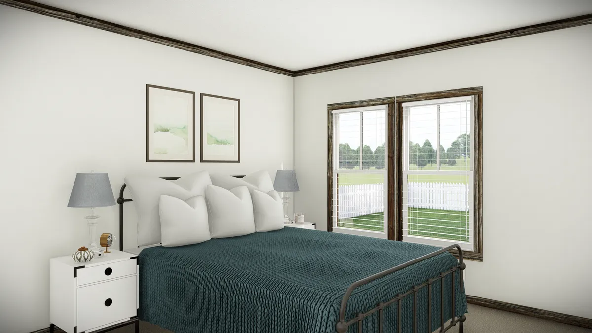 Bright bedroom with a metal bed frame, teal bedding, two nightstands with lamps, two wall art pieces, and large windows overlooking a grassy outdoor area.