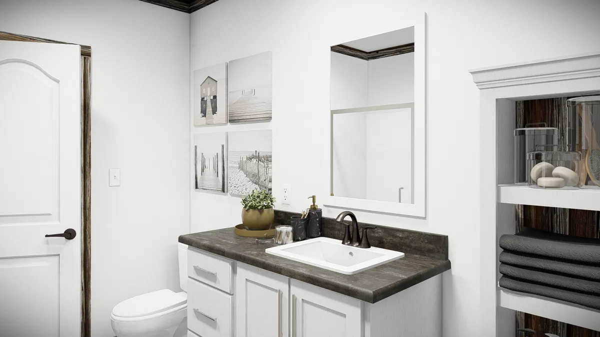 A modern bathroom with a white vanity, black faucet, wall-mounted mirror, toilet, and open shelving with towels and jars, plus decorative wall art above the toilet.