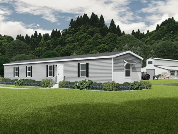 A gray manufactured home with white trim sits on a green lawn, with trees, a barn, tractor, and horses in the background under a partly cloudy sky.