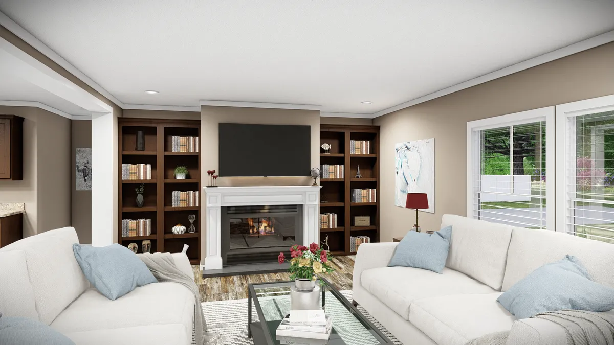 A modern living room with two white sofas, a glass coffee table, a fireplace with a TV above it, built-in bookshelves, and large windows letting in natural light.