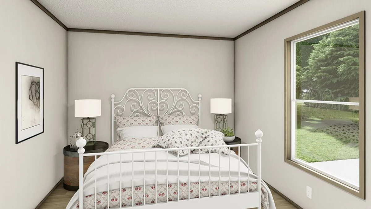 A neatly made bed with a decorative white metal headboard, two bedside tables with lamps, a framed picture on the wall, and a window overlooking a green yard.