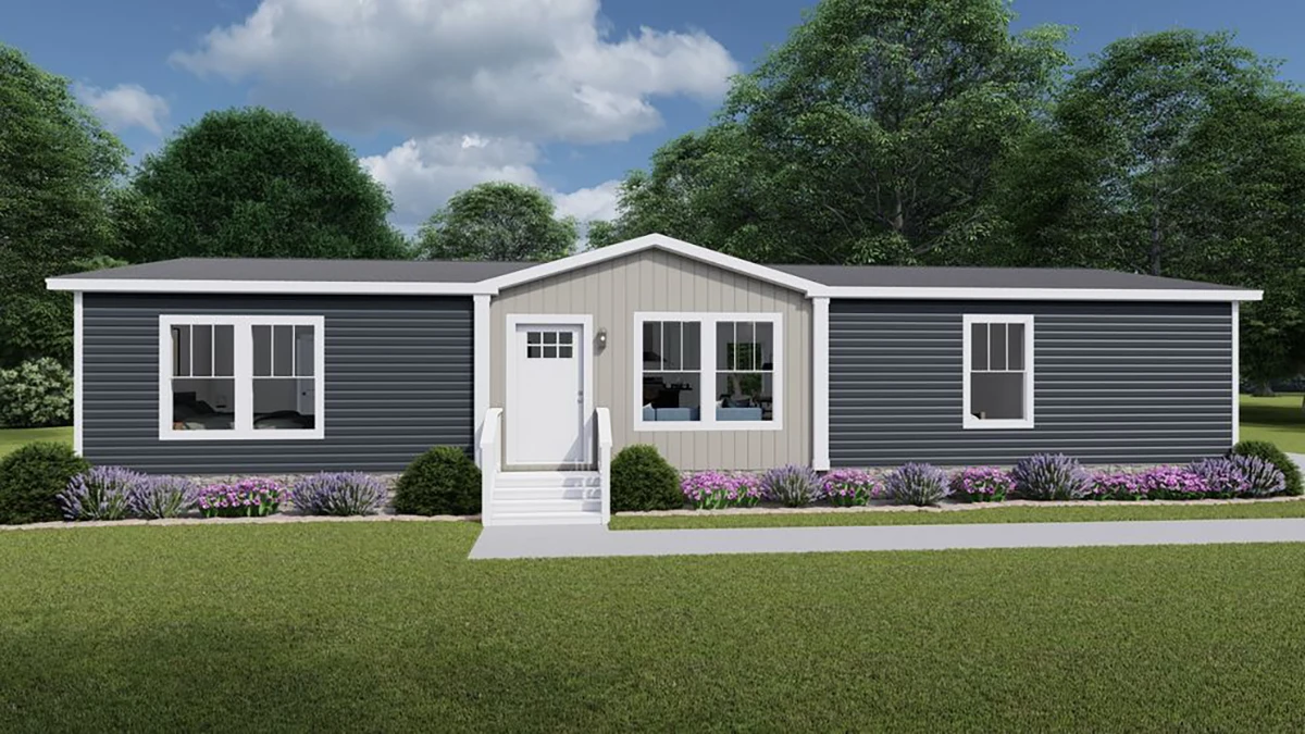 a2bcb8ab-5098-41d1-83be-1377dcae4169 A modern single-story manufactured home with dark gray siding, white trim, front steps, and landscaped shrubs and flowers, set against a backdrop of trees and cloudy sky.