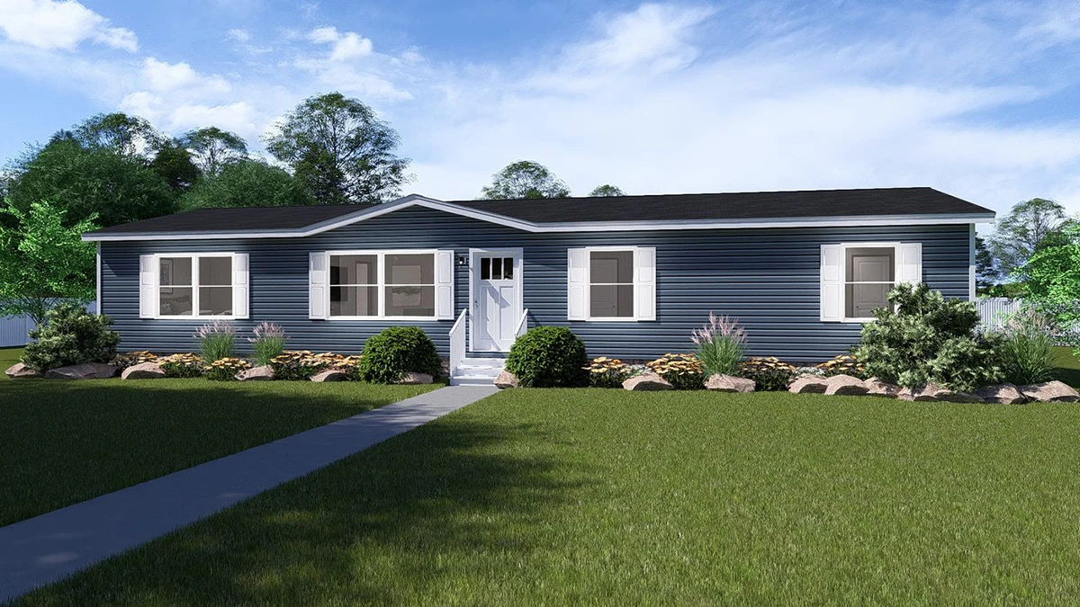 A single-story, blue manufactured home with white trim, a central front door, and a landscaped yard with shrubs and rocks under a partly cloudy sky.