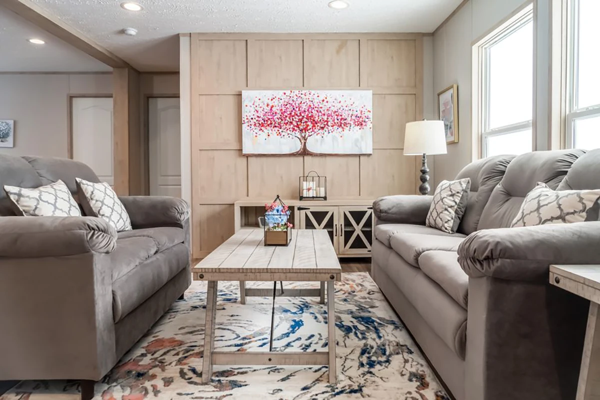 A living room with two gray sofas, a wooden coffee table, a lamp, large windows, and a wall art piece of a red-leafed tree above a sideboard.