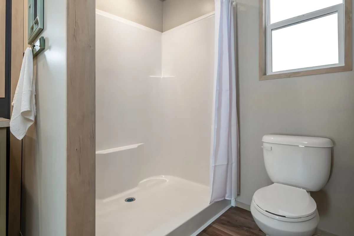Bathroom with a white shower stall with a curtain, a white toilet, towel on a rack, and a window on the wall.