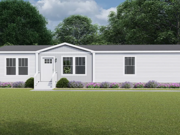 A white manufactured home with a gray roof, front steps, and simple landscaping sits on a grassy lawn with trees in the background under a partly cloudy sky.