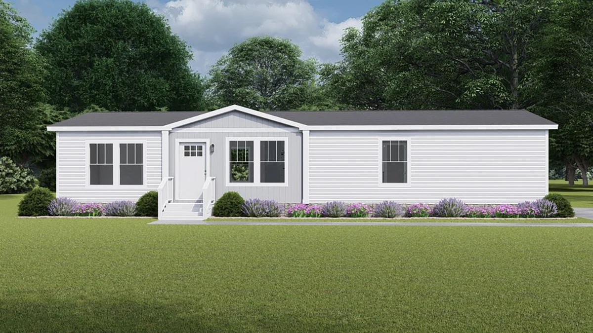 A white manufactured home with a gray roof, front steps, and simple landscaping sits on a grassy lawn with trees in the background under a partly cloudy sky.