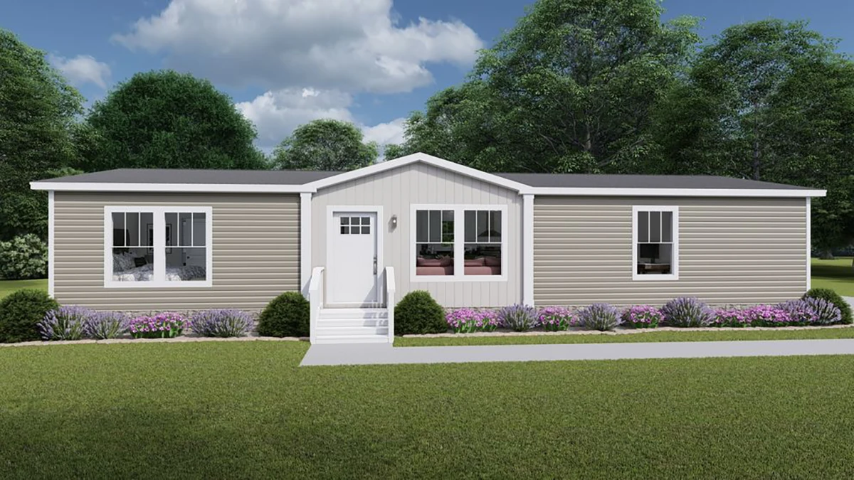 A beige manufactured home with white trim, three front windows, a central white door with steps, and landscaped bushes and flowers in front, set against green trees and a cloudy sky.