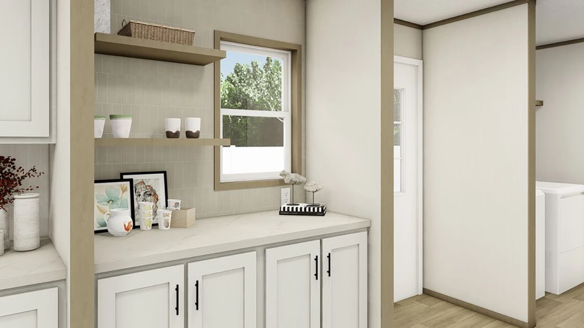 A kitchen counter with white cabinets, decorative items, shelves with cups, a window, and a door leading to another room.