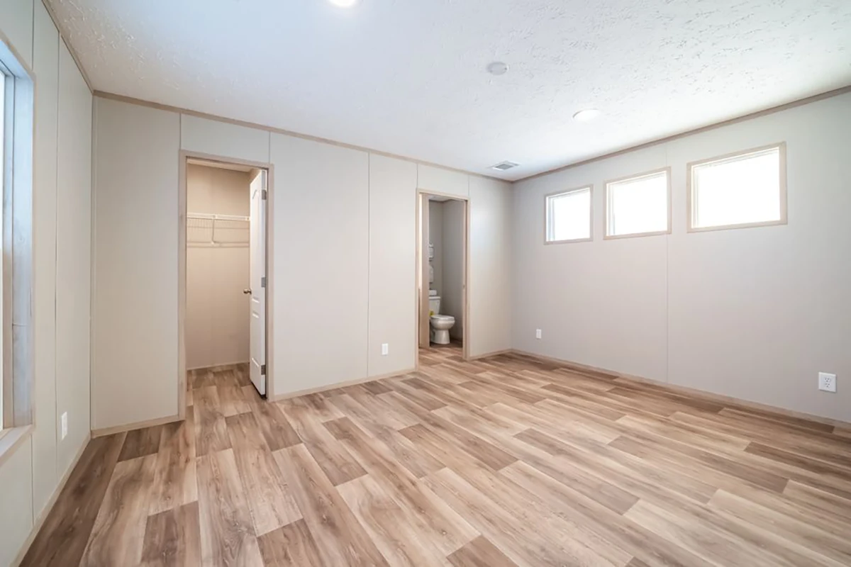 Empty room with light wood flooring, three high windows, a closet with an open door, and a bathroom visible through another open door.