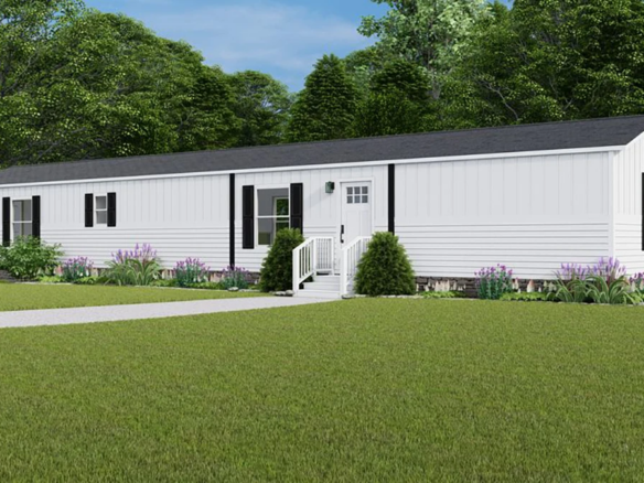 A white single-wide manufactured home with black shutters, a small front porch with steps, and surrounding landscaping, set on a grassy lawn with trees in the background.