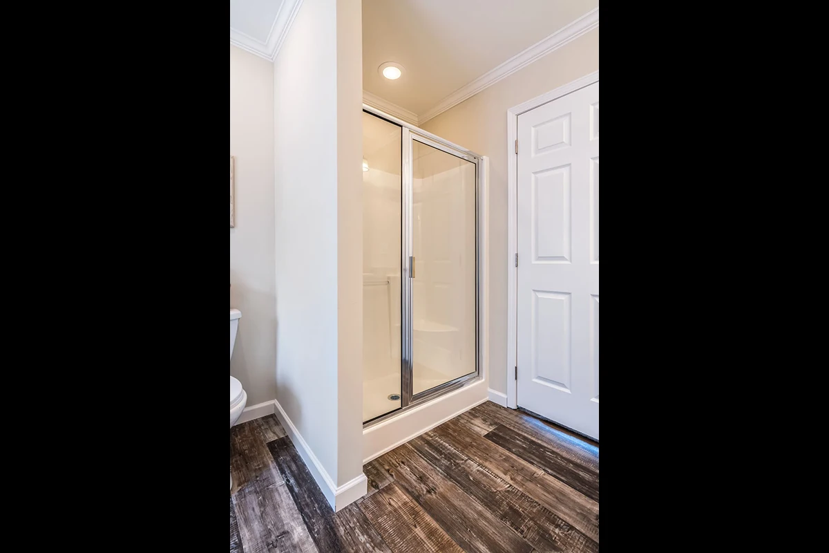 A bathroom with a glass-enclosed shower, wood-look flooring, beige walls, and a white door.