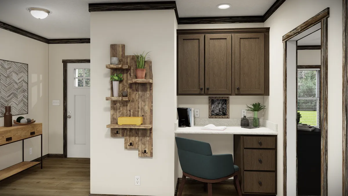c90d3fbf-268a-44b8-acfe-9735a3d06a1c A small home office nook with a built-in desk, brown cabinets, a green chair, plants, and a wooden wall shelf, next to a hallway and door.