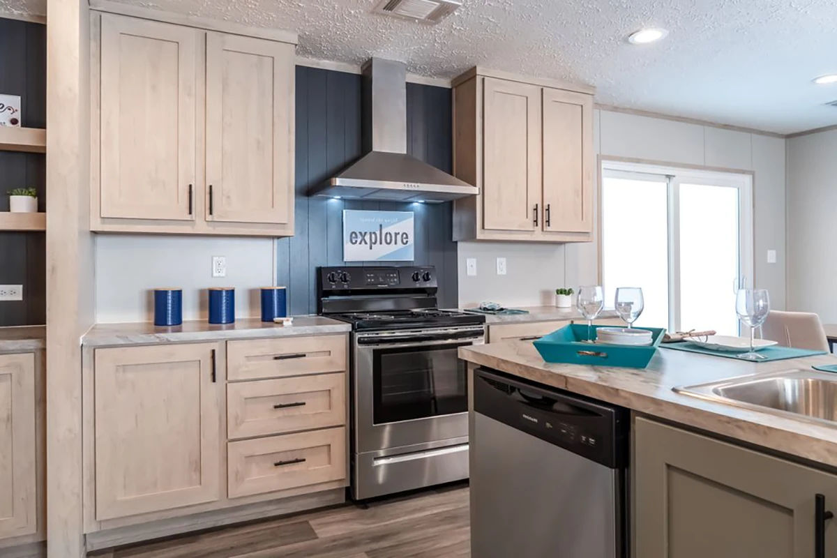 Modern kitchen with light wood cabinets, stainless steel appliances, a stove with a hood, dishwasher, and a decorative "explore" sign above the oven.