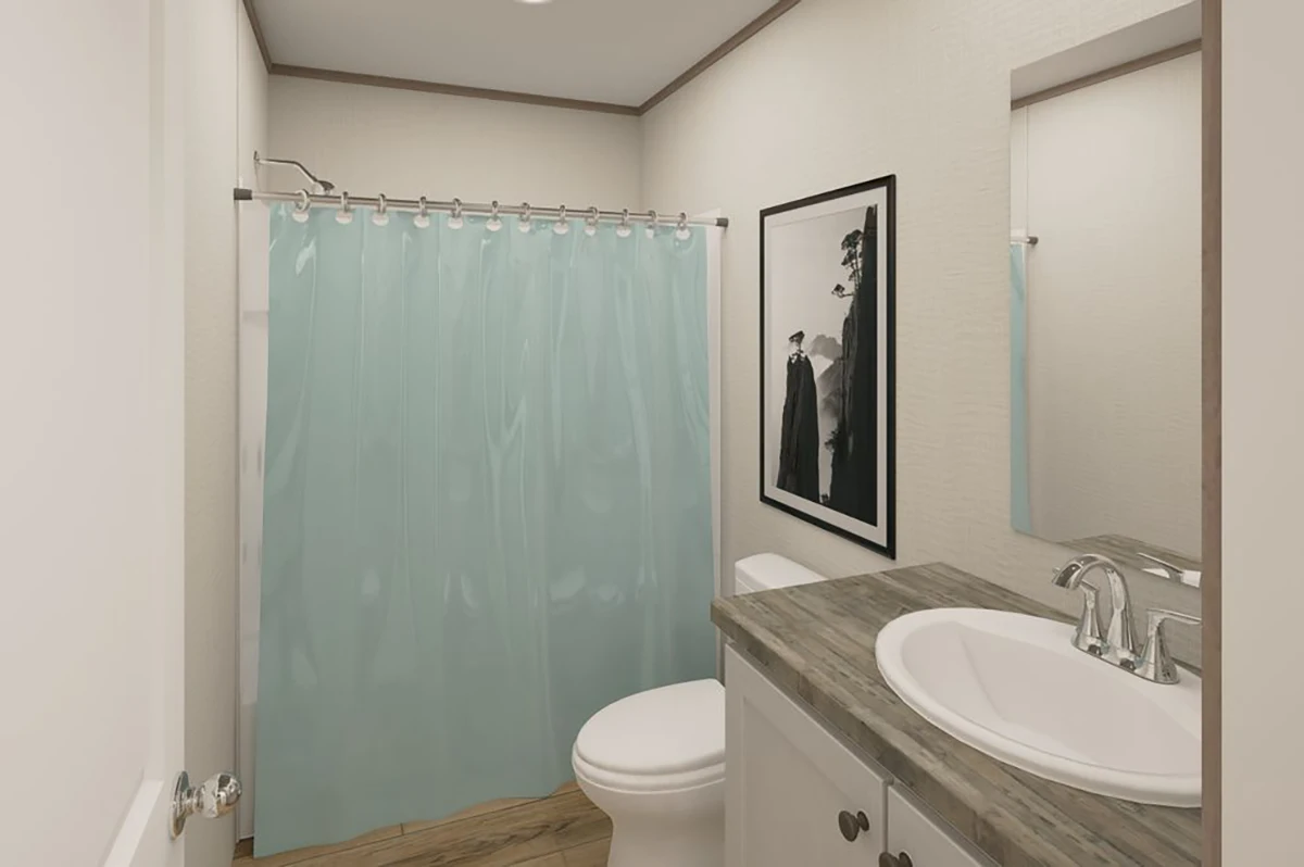 A small bathroom with a light blue shower curtain, a toilet, a sink with a counter, a mirror, and a framed black-and-white picture on the wall.