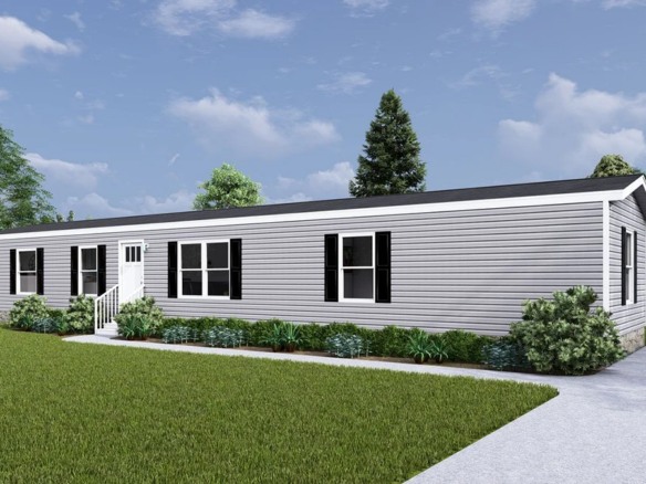 Single-story gray manufactured home with black shutters, white trim, small entry steps, landscaped shrubs, and a driveway, set against a grassy yard and trees under a partly cloudy sky.