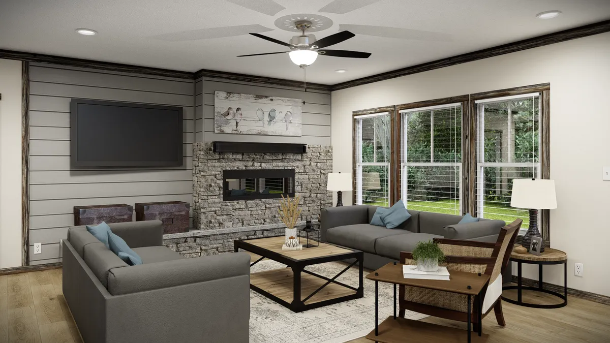 d21e7526-8f8e-4d19-876d-7259b2ffa8f0 A modern living room with gray sofas, a stone fireplace, wall-mounted TV, large windows, and wood accents. A ceiling fan and artwork are visible above the fireplace.