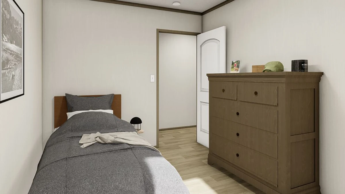 A small bedroom with a single bed, gray bedding, a wooden dresser, a lamp, and a door slightly open. A framed photo hangs on the wall.