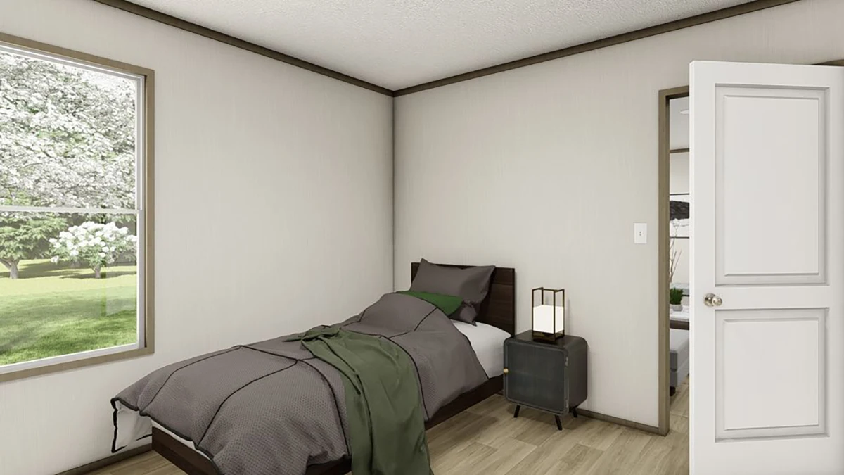 A small bedroom with a single bed, gray bedding, a nightstand with a lamp, an open door, and a window showing trees outside.
