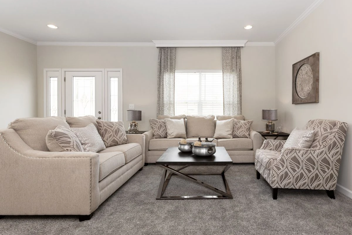 A neutral-toned living room with two beige sofas, an armchair, a black coffee table, two side tables with lamps, and a window with sheer curtains.