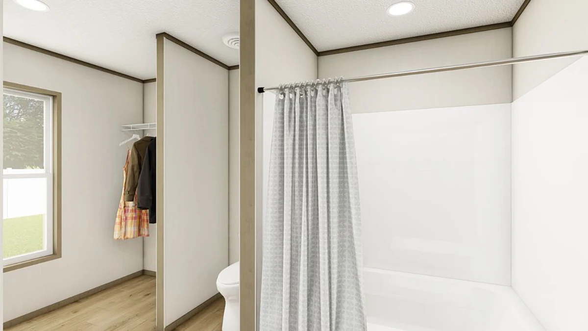 A bathroom with a white bathtub and gray shower curtain, adjacent to an open closet with clothing and a window letting in natural light.