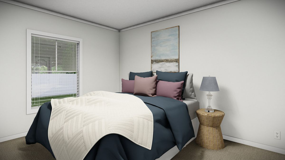 db87c3d1-b3c2-409a-998b-3f49acba5edf A neatly made bed with blue and white bedding, three pillows, and a cream throw blanket sits in a corner next to a wicker nightstand with a lamp; window and wall art visible.