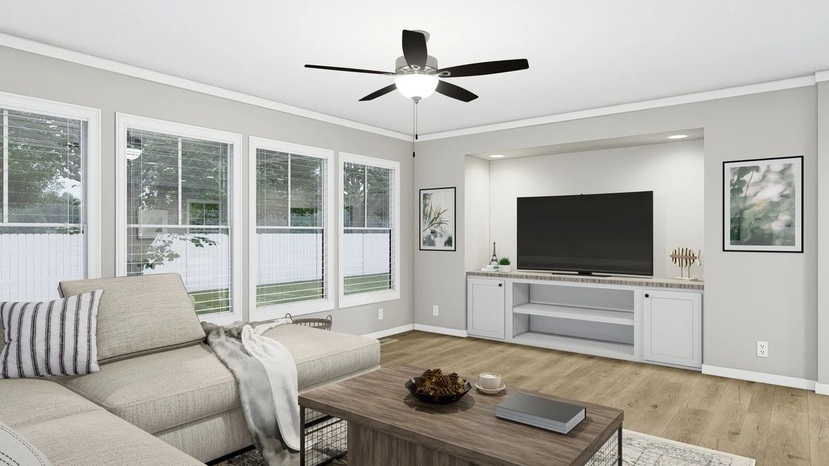 A modern living room with a beige sectional sofa, wooden coffee table, TV on a built-in unit, large windows, light gray walls, and a ceiling fan with a light.