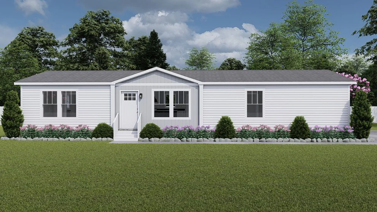 Single-story manufactured home with white siding, gray roof, multiple windows, front steps, and neatly landscaped bushes and flowers.