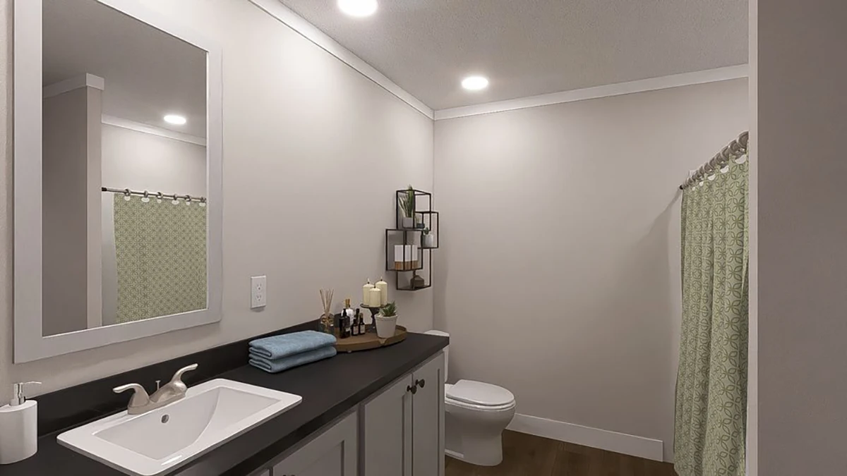 A modern bathroom with a sink, black countertop, folded towels, decorative items, a toilet, and a shower with a green patterned curtain.