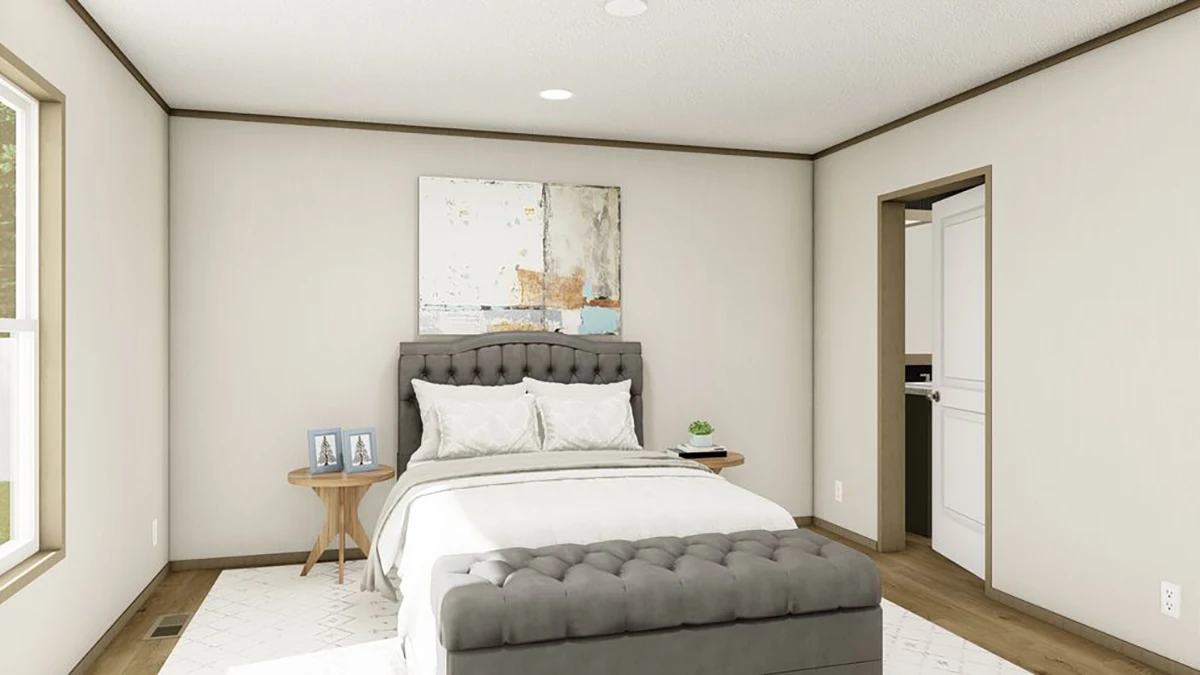 A bedroom with a gray tufted bed, white bedding, two wooden side tables, framed art above the bed, and a door leading to an adjoining room.