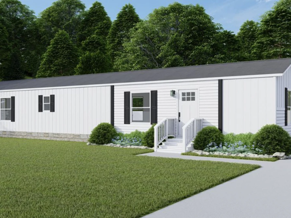 A white single-wide mobile home with black shutters, front steps, small shrubs, and a manicured lawn, set against a background of dense green trees.
