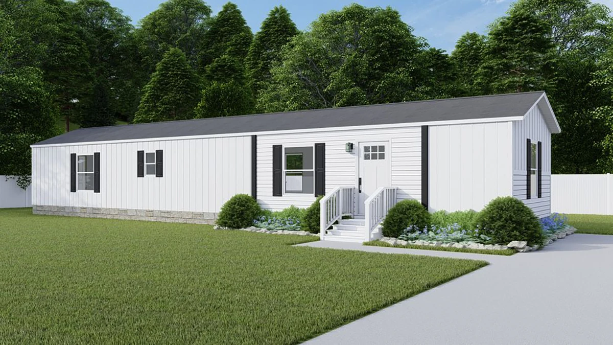 A white single-wide mobile home with black shutters, front steps, small shrubs, and a manicured lawn, set against a background of dense green trees.