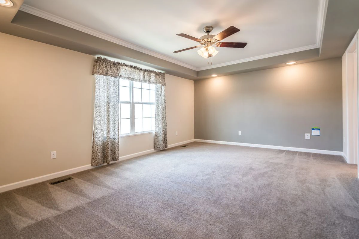 Empty carpeted room with beige walls, ceiling fan with lights, window with curtains, and recessed lighting in the ceiling.
