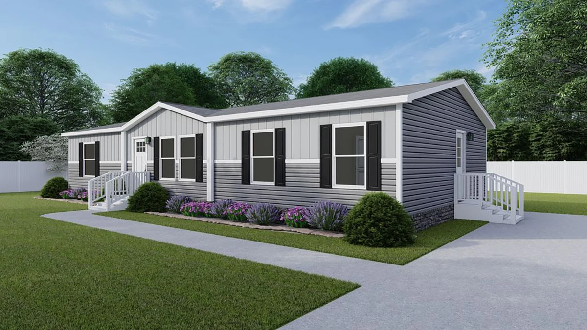 A single-story manufactured home with gray siding, white trim, black shutters, two entrances with steps, and flower beds in front, set on a lawn with trees and a white fence.