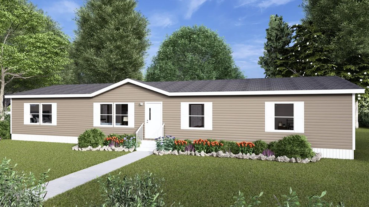 A single-story manufactured home with beige siding, white trim, a dark roof, a small porch, and a landscaped front yard with flowers and shrubs.