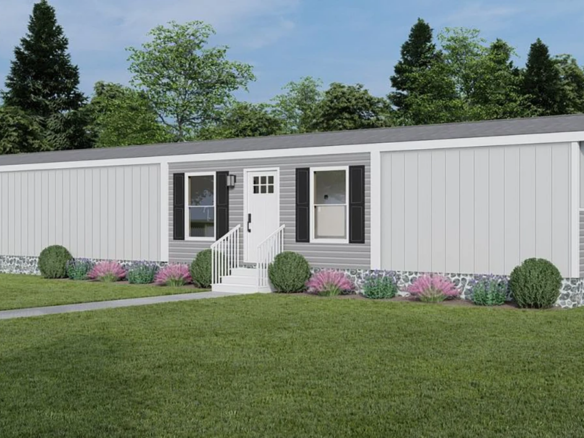 A gray manufactured home with white trim, front steps, landscaped shrubs, and a grassy lawn, set against trees and a blue sky.