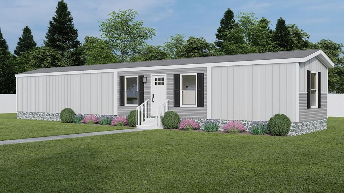 A gray manufactured home with white trim, front steps, landscaped shrubs, and a grassy lawn, set against trees and a blue sky.