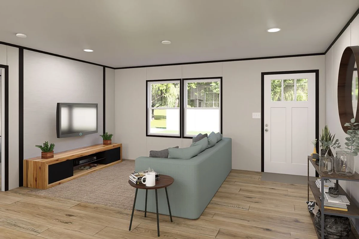 ec16bfd9-1a55-4c83-a405-9eb59c3cc580 A modern living room with light walls, wood flooring, a gray sofa, wall-mounted TV on a wooden console, and a windowed door. A round mirror and plants decorate a side table.