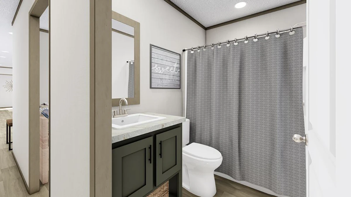 A modern bathroom with a sink, mirror, toilet, and bathtub with a gray shower curtain. A framed picture hangs on the wall above the toilet.