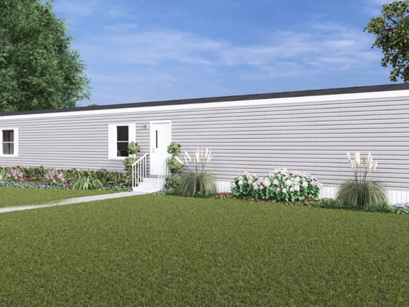 A single-story, gray manufactured home with white trim, surrounded by a lawn, shrubs, flowers, and a white picket fence under a blue sky.