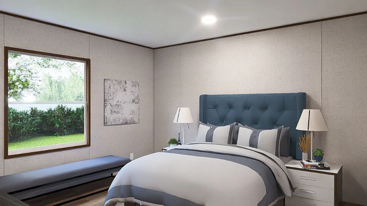 A bedroom with a blue upholstered headboard, white and gray bedding, two bedside tables with lamps, a bench by the window, and a painting on the wall.