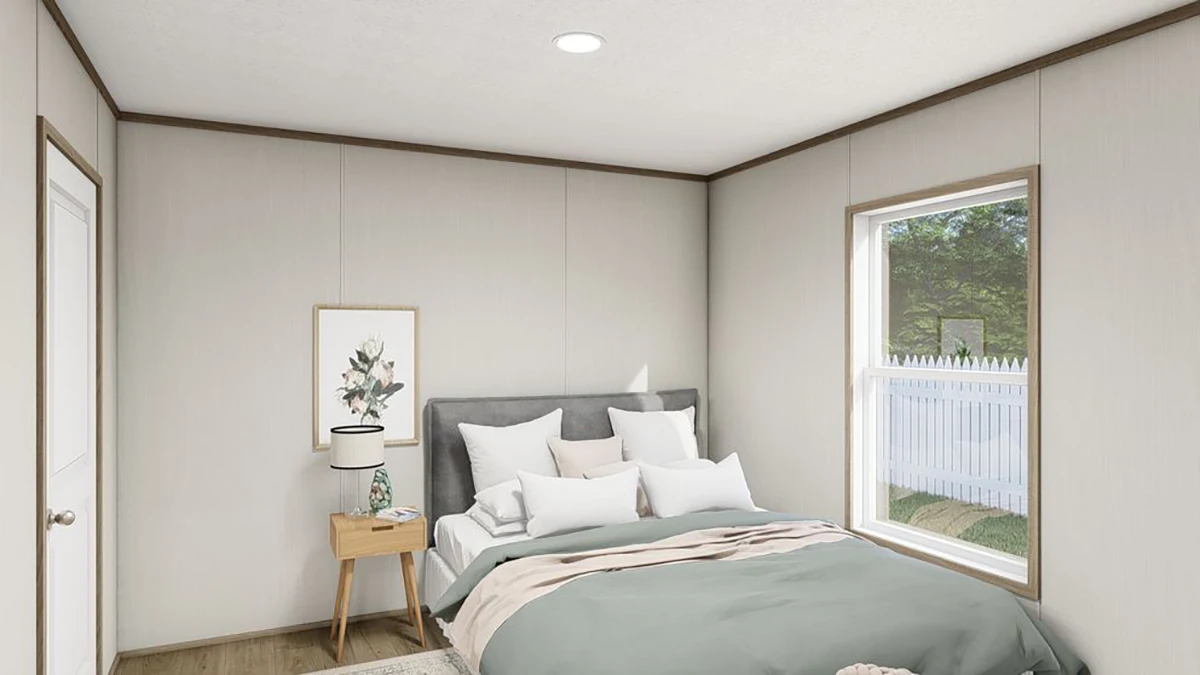 ed8be173-8113-4b26-adcd-4243601c84db A small bedroom with a bed, nightstand, lamp, framed picture, and a window showing a white fence and greenery outside.