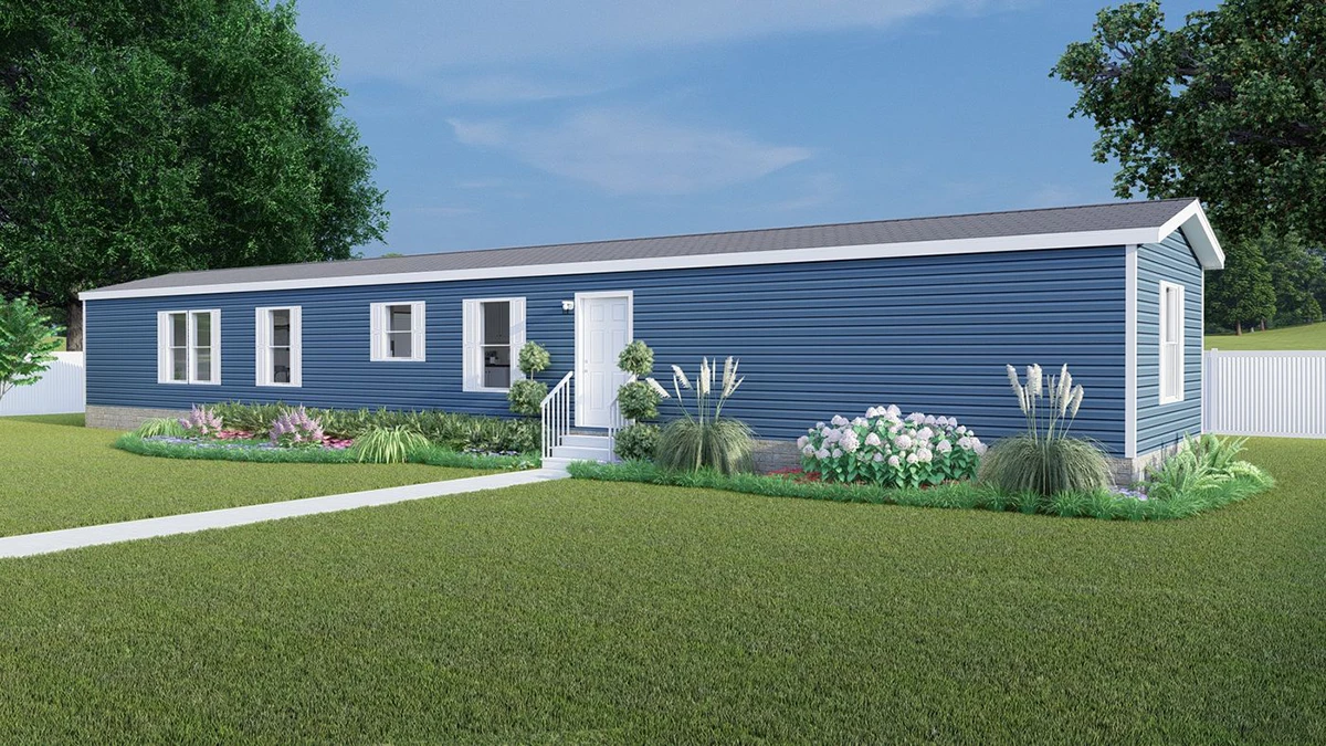 A blue single-story manufactured home with white trim, a central front door, several windows, and landscaped garden beds in a grassy yard.