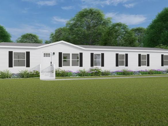 A single-story white manufactured home with black shutters, front steps, and a landscaped yard, set against green grass and trees under a blue sky.
