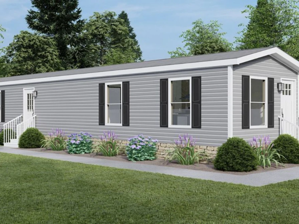 A gray manufactured home with white trim, black shutters, and steps at both entrances, surrounded by green grass, shrubs, and small purple flowers.