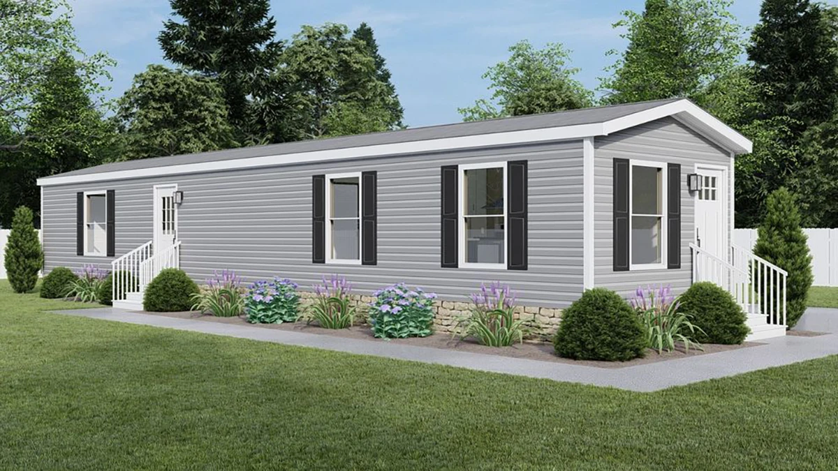 f1928793-8312-40b4-9284-99caf0d963b1 A gray manufactured home with white trim, black shutters, and steps at both entrances, surrounded by green grass, shrubs, and small purple flowers.