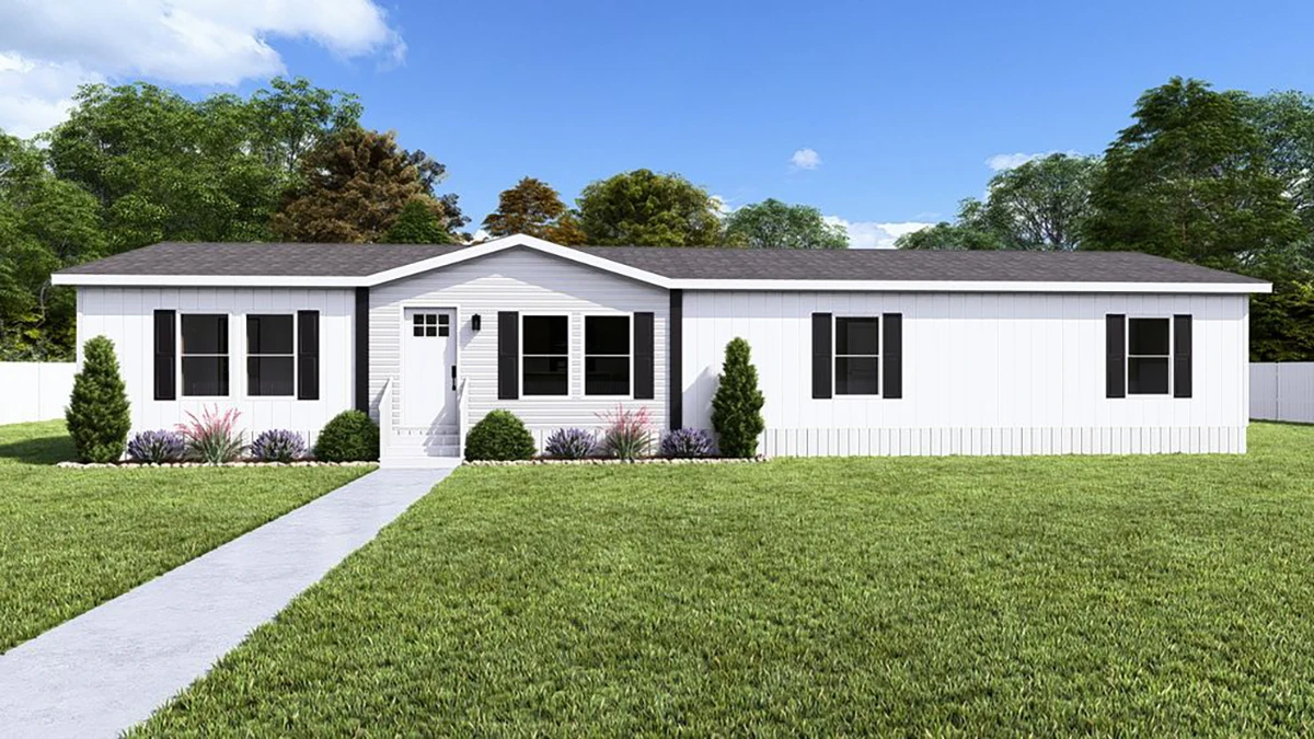 Single-story white manufactured home with black shutters, a central front door, shrubs along the foundation, and a concrete walkway, set on a grassy lawn with trees in the background.