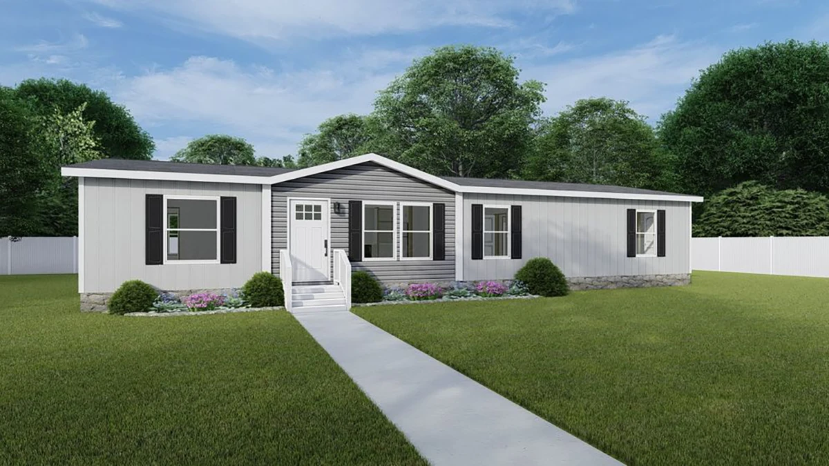 A single-story manufactured home with gray siding, black shutters, a small front porch, and a concrete walkway, surrounded by a green lawn and landscaped shrubs.
