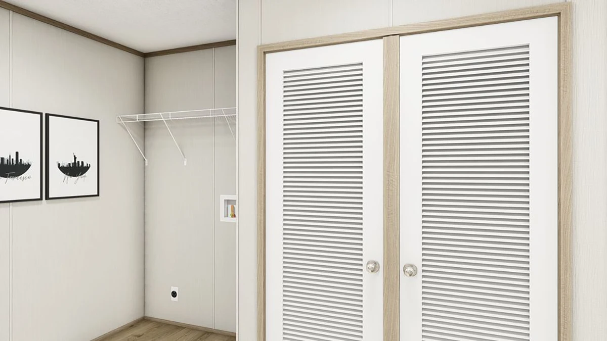 f3bb7bd9-d362-49c3-a365-73b807a55117 A small empty room with a wire shelf, two framed pictures on the wall, and closed white double closet doors with horizontal slats.