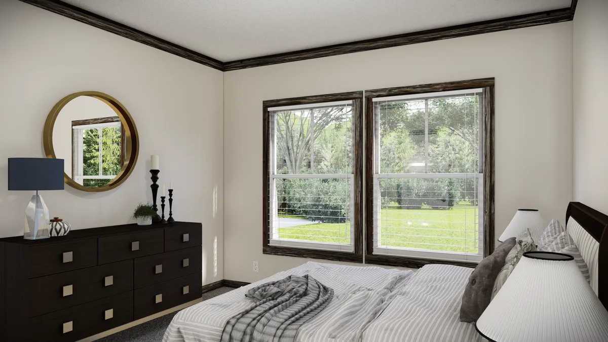 f5120889-6255-4b87-8582-775c7129d0b3 A bedroom with a bed, striped bedding, a dark wood dresser with a round mirror, lamp, candles, and two large windows showing a green yard outside.
